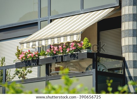 Balcony with awning opened and beautiful flowers - covered by sun-shield on a warm summer day