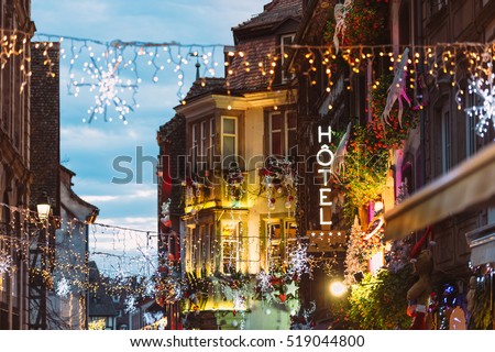 Hotel neon sign on romantic luxury building above colorful Christmas Market atmosphere with people silhouettes Christmas toys and decorations in oldest Christmas Market worldwide, Strasbourg