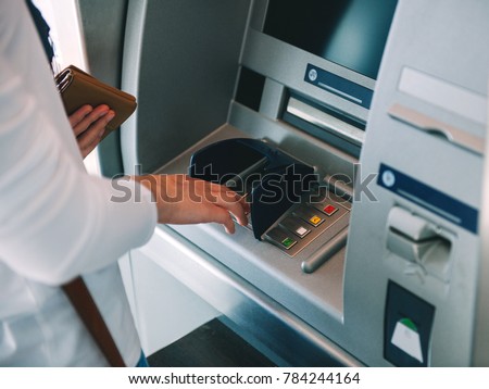 Woman using ATM holding wallet an pressing the PIN security number on the keyboard automatic teller machine
