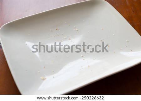 close up look of white rectangular plate with some food stain and small bread crumb on brown wooden table