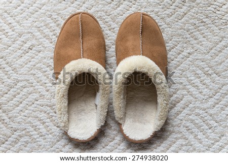 a pair of brown suede winter slipper on the light grayish brown color area rug