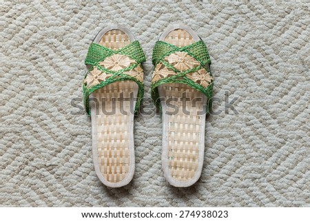 a pair of light brown and green hand weaved woman slipper on a light grayish brown area rug