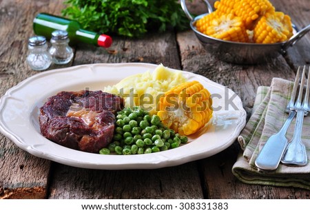 Rare beef steak with mashed potatoes, green peas and boiled corn