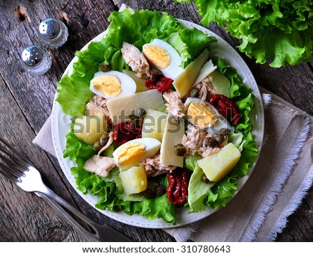 salad of lettuce, iceberg lettuce, with canned tuna, dried tomatoes, boiled potatoes, capers and parmesan cheese, dressed with olive oil. Selective focus. rustic style.