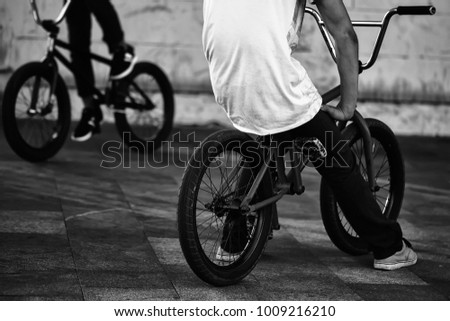 Legs of two teenager boys sitting on orange and black bmx low bicycles on street summer male sports activity outdoor closeup on natural background, horizontal picture