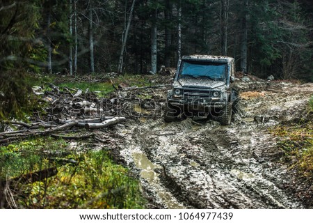 Dirty offroad car with dark forest on background. SUV covered with mud on countryside road. Crossover racing on sunny day. Extreme entertainment and driving concept.