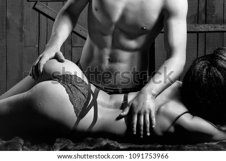 Sexy young undressed sensual woman with beautiful straight body in red lace erotic lingerie lying near muscular man touching buttocks posing indoor on wooden background, horizontal picture
