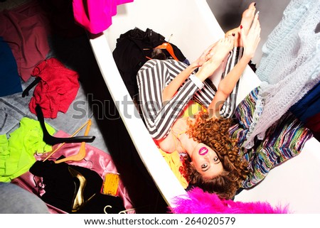 Beautiful fashionable crazy woman with curly hair in bathtub with colorful clothing