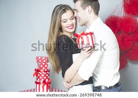 Romantic couple of lovers embraces, laughing and standing close to each other holding gift, horizontal photo