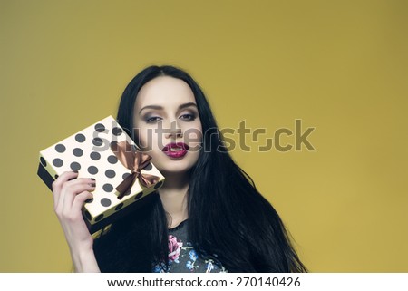 Beautiful smiling girl holding square present box on yellow background, horizontal picture