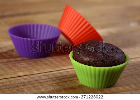 Brown chocolate cupcake in colored silicone bakeware red violet and green colors on wooden table top, horizontal photo