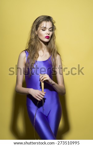Pensive slim girl in violet second skin jumpsuit standing with tape-line on yellow background, vertical picture