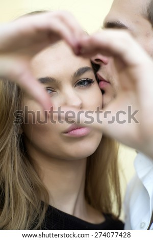 Attractive young couple, girl holding hands in a shape of heart and boy kissing the girl, vertical picture