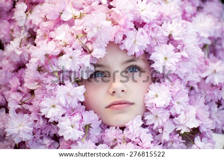 Face of small girl with opened blue eyes among pink flowers of japanese cherry blooming copyspase, horizontal picture