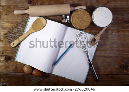 Set of ingredients and appliances for cooking with opened recipe book on wooden table top, horizontal picture