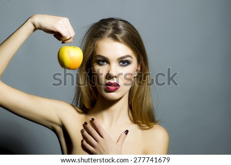 Passionate sensual woman with bright make up looking forward holding fresh yellow apple standing on gray background copyspace, horizontal picture