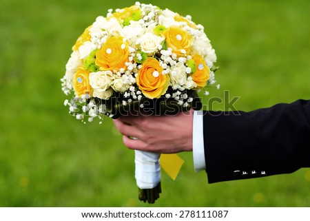 Fiance holding a bright wedding bouquet of white and yellow roses outdoor on green natural background, horizontal picture