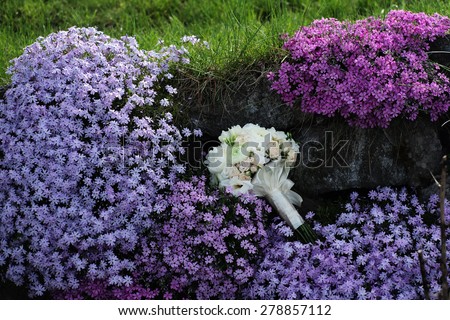 Beautiful delicate wedding bouquet of roses and peony in pastel colours lying among purple and violet flowering bushes  in broad daylight outdoor on natural background, horizontal picture
