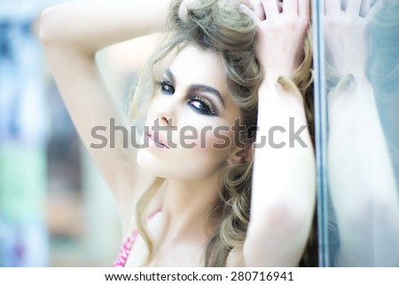Soft colors portrait of beautiful young woman with bright make up touching her curly hair looking forward, horizontal picture