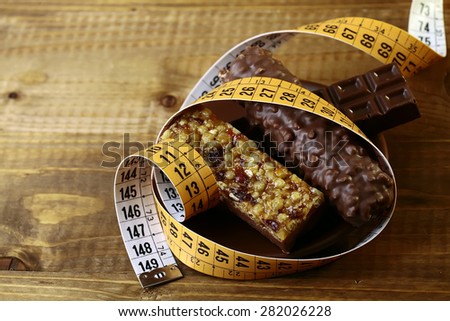 Delicious chocolate bars and peanut brittle with a measuring tape as a symbol of diet on brown wooden table top background, horizontal photo