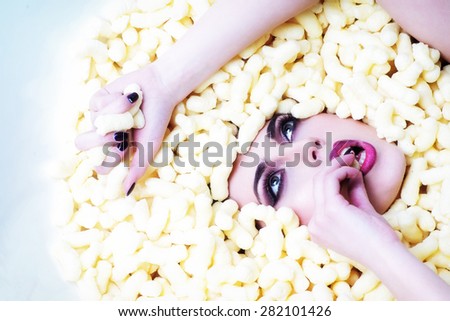 Portrait of fashionable young beautiful girl face in corn sticks heap in bathtub tasting and looking away on light food background copy space, horizontal picture