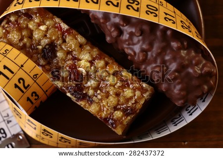 Tasty chocolate bars and peanut brittle with a measuring tape as a symbol of diet closeup, horizontal photo