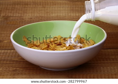 Sweet krispy of cereal cornflakes with frosting in light green plate and spoon filling in with milk from plastic bottle on brown wooden table top background, horizontal photo