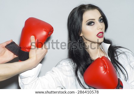 Sexual strong brunette girl with bright makeup in white blouse and red boxing gloves standing on light grey backdrop, horizontal picture