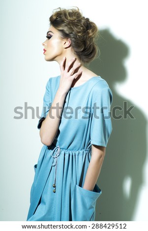 Attractive fashionable woman with bright makeup and chignon in light blue dress standing on white background, vertical picture