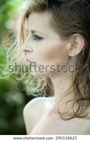Portrait of slender young woman profile with blonde short hair standing on natural background, vertical picture