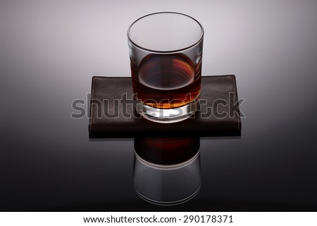 One glass cup with strong amber alcoholic drink reflecting and standing on brown leather napkin on grey and white background, horizontal picture