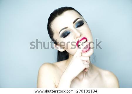 Nude vamp brunette girl with bright makeup biting finger standing on light grey background copyspace, horizontal picture