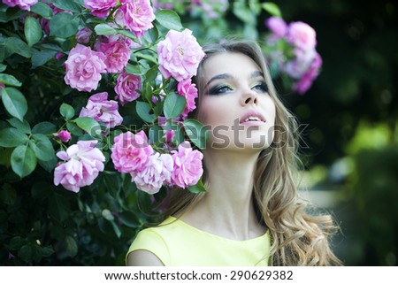 Portrait of alluring thoughtful young blonde woman with bright makeup and curly hair with lush bush of pink rose, horizontal picture