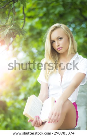 Attractive sweet blond woman sitting outdoor with book in summer on green natural background, vertical picture