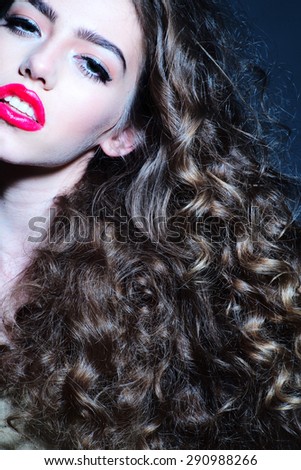 Passionate pretty young girl with beautiful curly hair and bright pink lips looking forward standing with open mouth on dark background, vertical picture