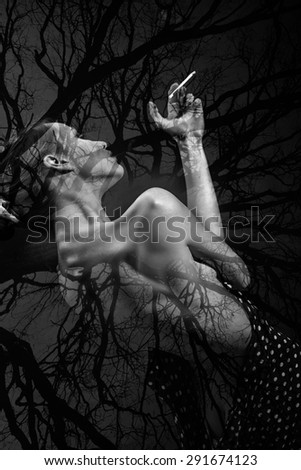 Pretty sexy naked young woman with straight beautiful body with bare tree texture smoking standing with back on natural background black and white, vertical picture