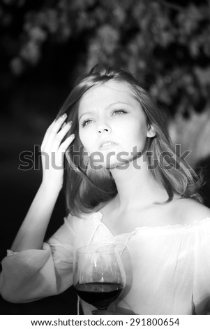 Portrait of thoughtful attractive young girl with wine glass standing outdoor in sunset on natural background black and white, vertical picture