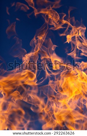 Beautiful bright wild orange yellow tongues of flame from a fire outdoor on clean blue sky background, vertical picture