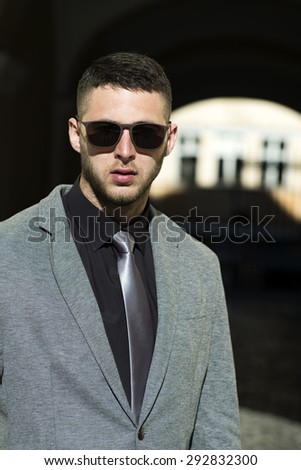 Handsome sexual man in sunglasses formal grey jacket and gray tie standing on outdoor backgroung, vertical photo