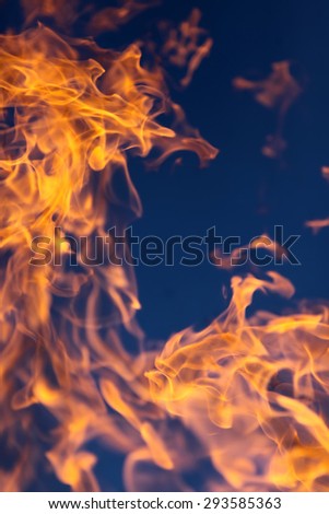 Scary bright hot orange yellow tongues of flame from a fire outdoor on clean blue sky background, vertical picture