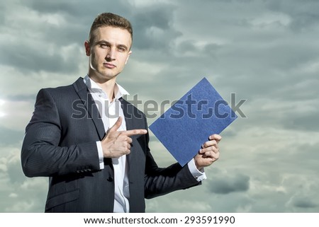 Serious attractive man in formal suit holding sheet of paper standing on blue sky background copyspace, horizontal picture