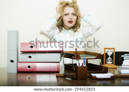 Emotional beautiful young woman has stress touching head sitting at table with heap of folders documentas and office supplies on white background, horizontal picture
