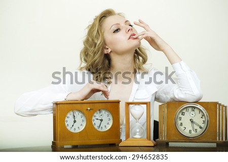 Pensive sexy blonde beautiful woman sitting with three different time measurements of sand glass and clock in formal clothes on white background, horizontal picture