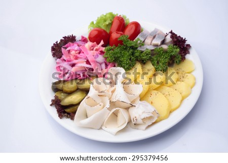 Restaurant food of variety diner platter of marinated cucumbers tomatoes sauerkraut lard herring and rings boiled potatoes decorated with lettuce and parsley isolated on white, horizontal picture