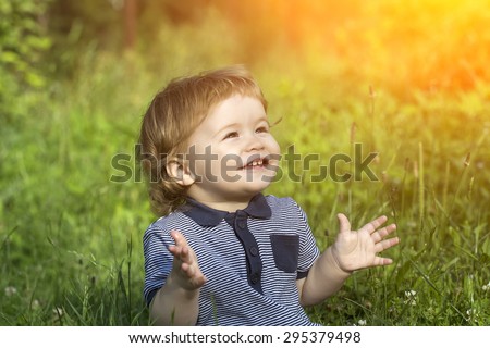 Little cute happy smiling baby boy sitting in field on fresh green grass sunny day, horizontal picture