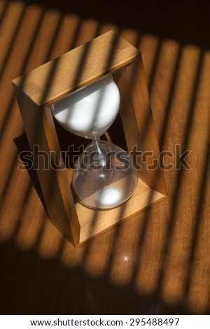 One old fashiouned wooden hour glass clock with white sand standing on table top in jalousie shade, vertical picture