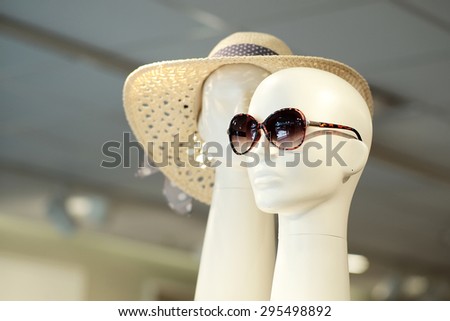 Two white plastic mannequin heads in sunglasses and summer hat indoor on shop background, horizontal picture