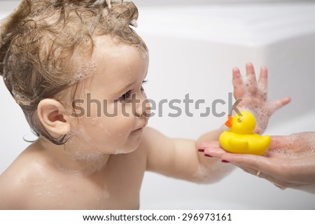 Cute little boy takes out of mom\'s hands yellow rubber duck in bubble bath, horizontal photo
