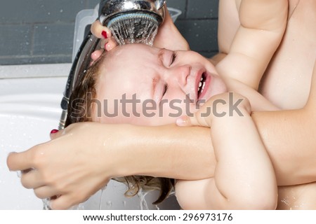 Closeup of small crying child on his mother\'s hands washing with water his head in shower in bathroom, horizontal picture