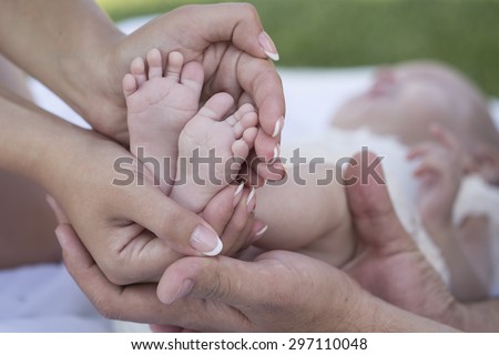 Happy family of mother and father holding bare feet with small toys and soft skin of little tiny baby with male and female hands outdoor closeup, hotizontal picture
